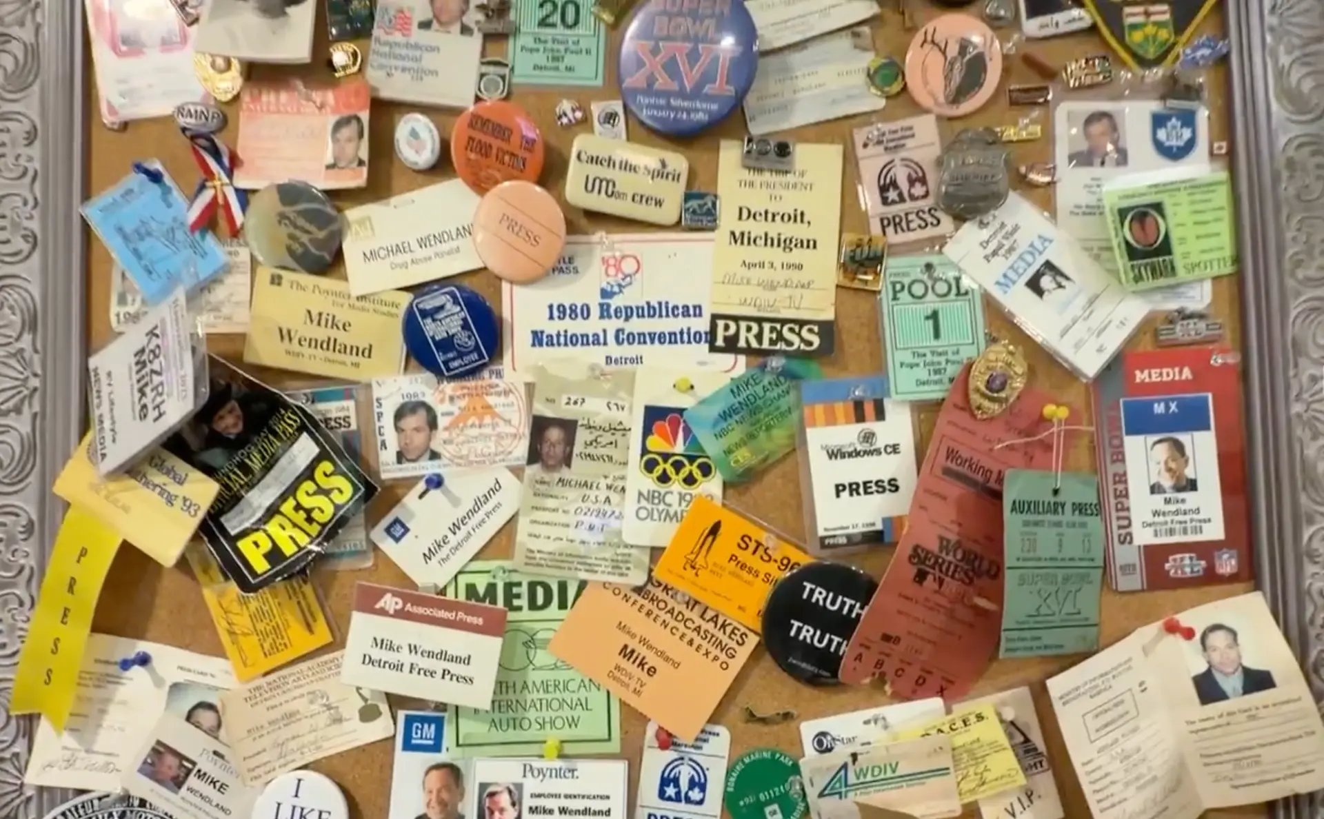 A bulletin board covered in decades of press passes, media credentials, and convention badges