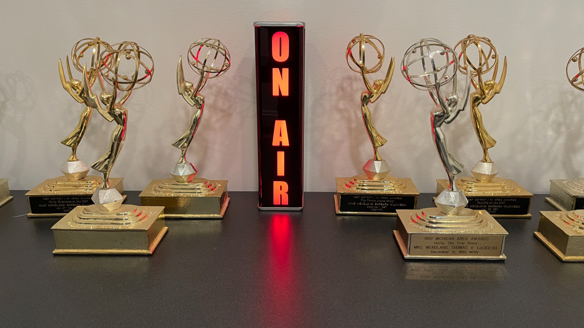 A lineup of Emmy Awards around a glowing ON AIR sign, plaques naming the WDIV investigations that won them